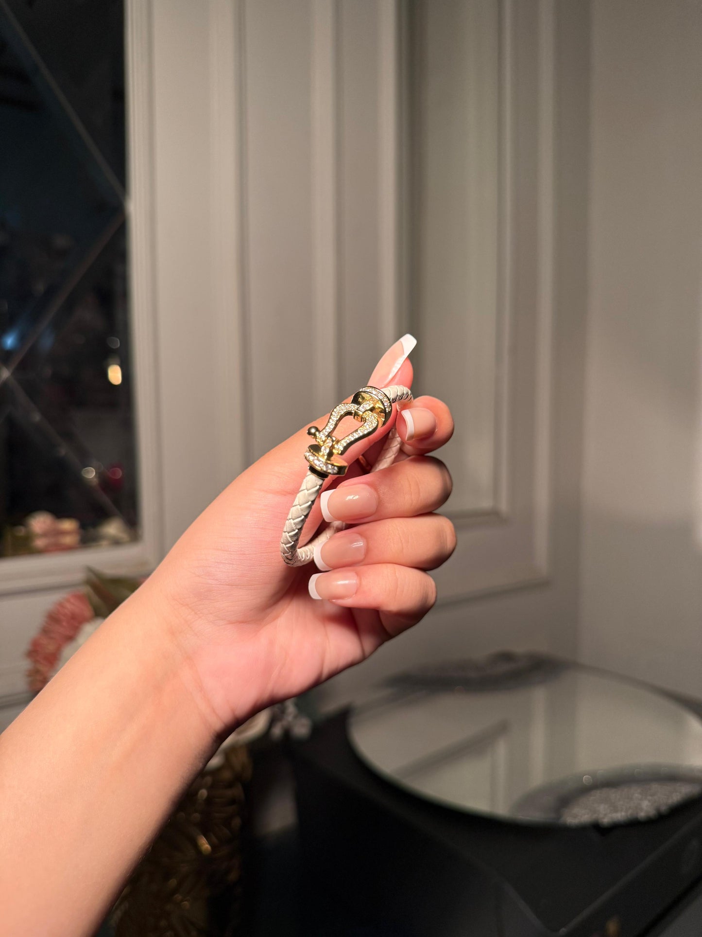 white braided leather bracelet with a gold crystal-encrusted buckle clasp.
