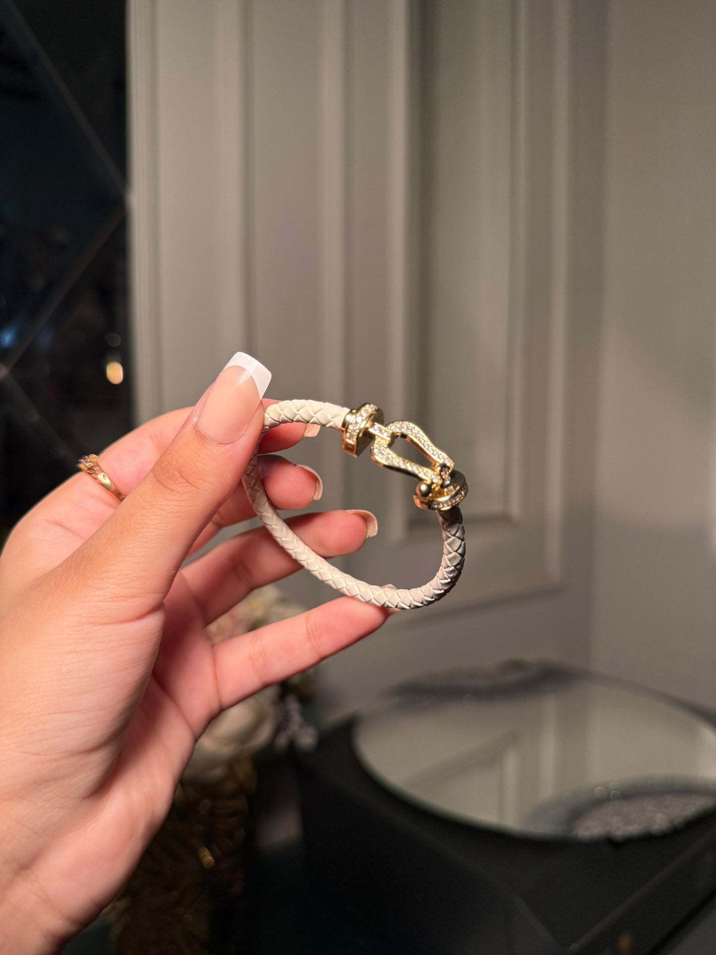 white braided leather bracelet with a gold crystal-encrusted buckle clasp.