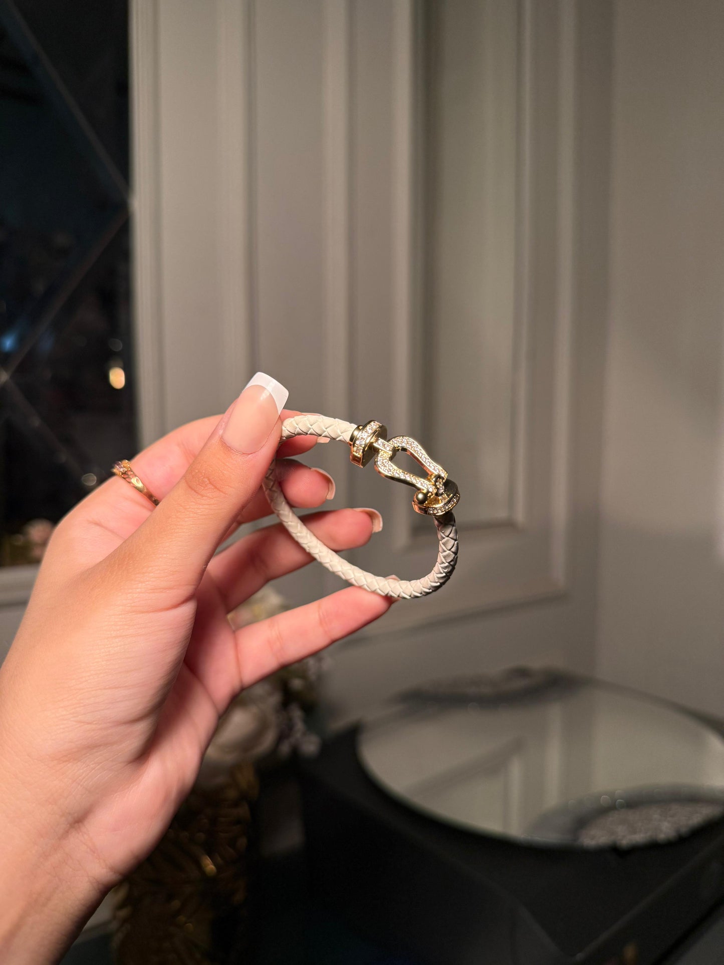 white braided leather bracelet with a gold crystal-encrusted buckle clasp.