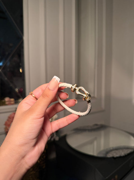 white braided leather bracelet with a gold crystal-encrusted buckle clasp.